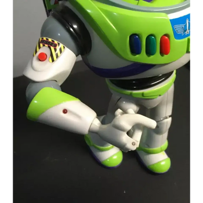 Close-up of Buzz Lightyear action figure's right arm, featuring a red laser button with a 'LASER' sticker on the upper arm and a blinking light further down.