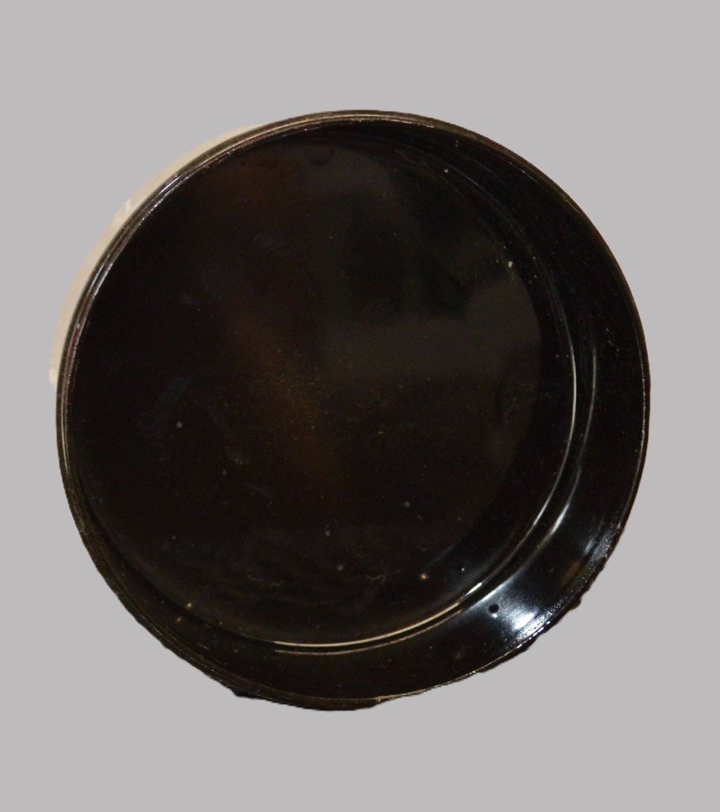 The interior of the same round box is shown, revealing a smooth, shiny black surface. The box is empty, and the lid has been removed to display the inside. It is placed on a green surface.