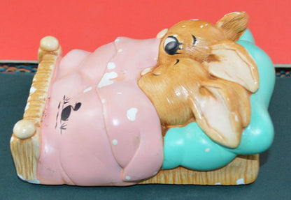 "Close-up of a Pendelfin figurine featuring two rabbits under a pink blanket with a black duck illustration.TMD167207